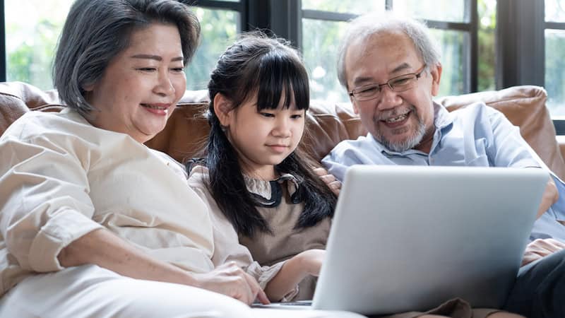 grandparents and granddaughter sitting together on a sofa and looking at a laptop, perhaps playing puzzles - like this week's Jumble puzzles with bowling and math