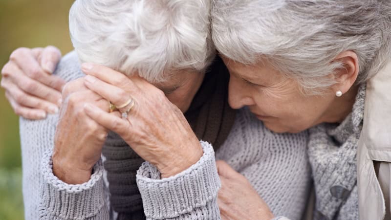 Two older women friends hugging to console each other in sadness. Image by Yuri Arcurs. Ask Amy column saying to reach out to friends in need