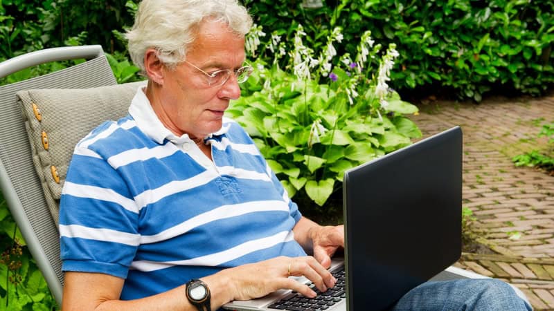 A senior man on a laptop outside, possibly doing a puzzle, like the Boggle the Birdies word search puzzle