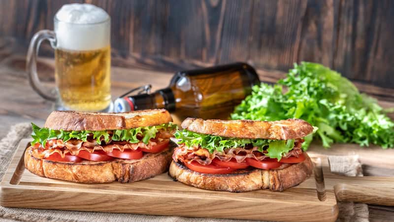 Tomato and Beer Pairings: Two BLT sandwiches in the foreground on a cutting board, a mug of beer in the background. By Alexpro9500