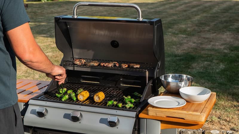 Man cooking meats and vegetables on a grill outside. If you plan to grill, take steps to do so safely. These healthy grilling tips can help.