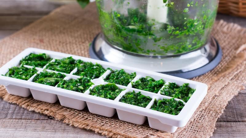 chopped herbs in a food processor and ice cube tray, demonstrating ways to repurpose food scraps. You might be surprised by some of the ingredients, like leftover herbs, that ended up on this list.