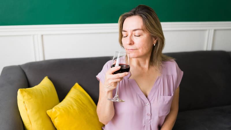 A woman closes her eyes as she sips from a glass of red wine. Image by Antoniodiaz. Used with spouses' drinking differences advice column.