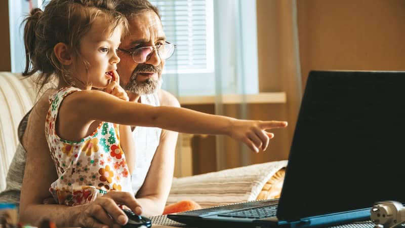 A little girl and her granddad looking at a computer screen, perhaps even doing a puzzle like this week's Jumble puzzles with skunks and a race