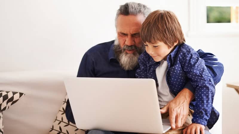 A granddad and grandson looking at a laptop together, perhaps doing a Kids Jumble puzzle