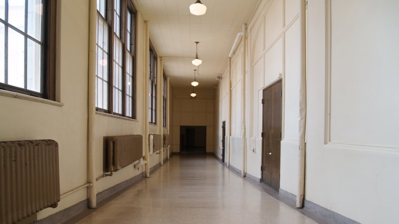 An old high school hallway, with windows, radiators, and hanging pendant lights. By Lisa Cora Reed