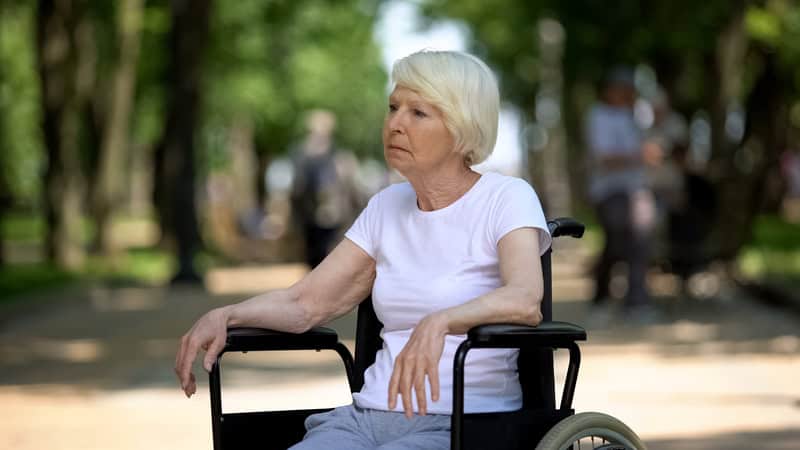 A sad woman sitting in a wheelchair outside in a park. Image by motortion. Used with advice column on showing up for disabled friends.