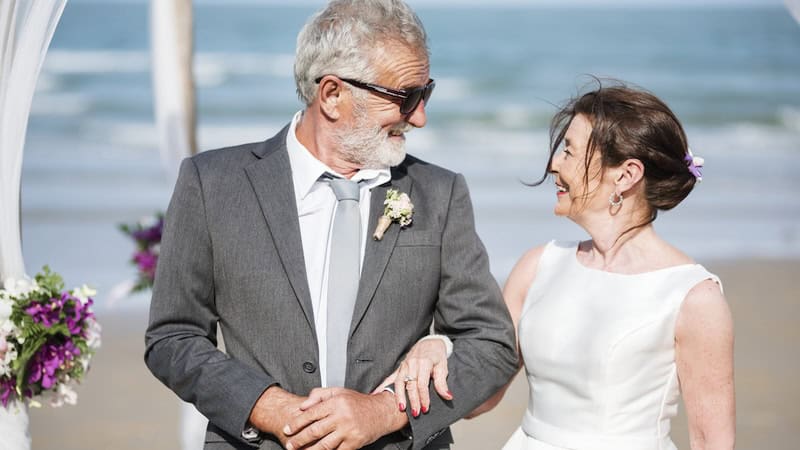 A senior couple getting married on the beach, possibly a practical wedding but still done with love.