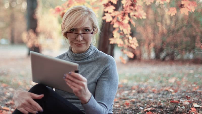 woman on a tablet, perhaps playing a puzzle. In an autumn outdoor setting