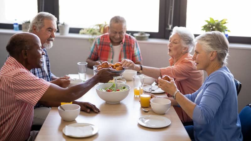 senior friends eating together, illustrating the loneliness-health connection