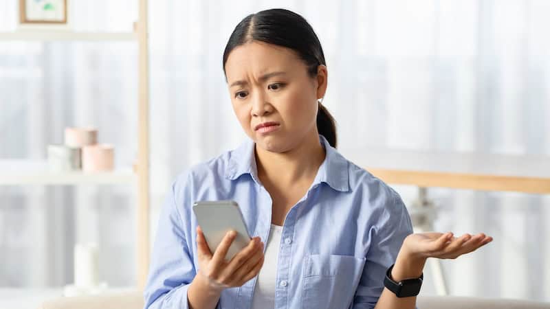 A woman looks with disgust and disappointment at her smartphone after a flaky friend has backed out on her.