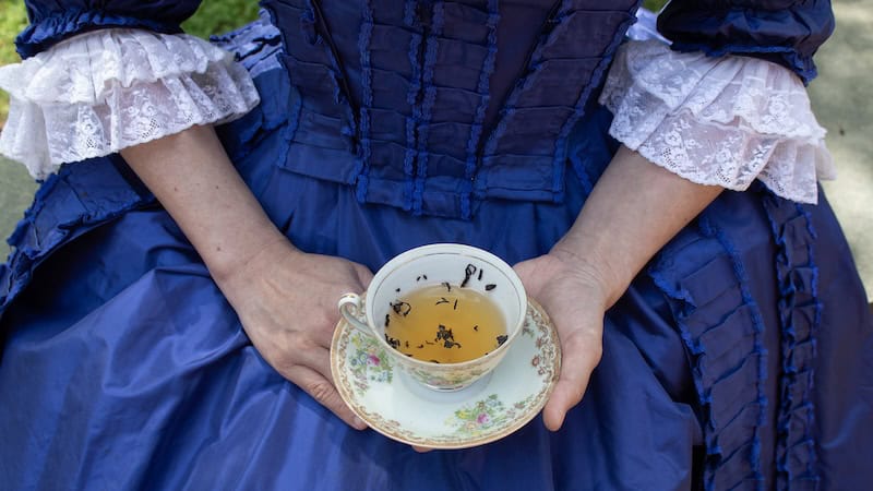 Woman in colonial garb holding a cup of tea. For the Colonial Tea Ball in Yorktown. Used in What's Booming November 7 - 14