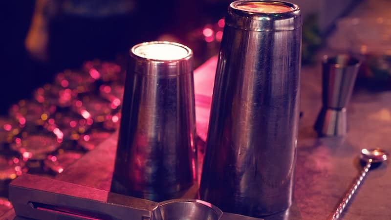 Red tinged light floods barware - a shaker, stirrer, glasses and more, reflecting the ideal of youthful memories of parents' parties