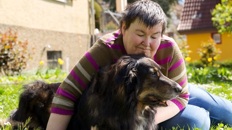 A disabled adult sits on the lawn hugging a happy dog. Illustrates the concept of the future of a disabled child. Image by Miriam Doerr