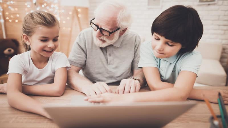 Granddad with two grandkids, together using a laptop, perhaps even doing a Jumble Kids puzzle