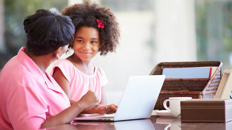 grandma and granddaughter on a laptop, perhaps doing puzzles like the Jumble Classic and for kids. Image by Monkey Business Images