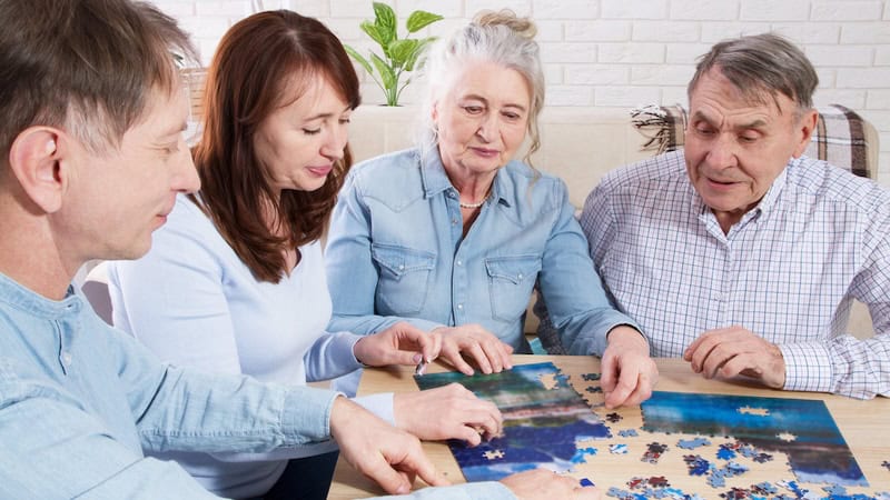 Two generations of a family doing a jigsaw puzzle together, illustrating two memory improvement strategies: tackling mentally challenging tasks and being socially engaged. By Pavelzhuravlev92