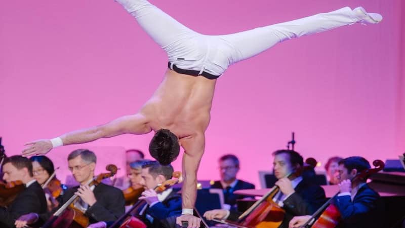 Cirque Musica with acrobat doing handstand as orchestra plays, as part of What's Booming, Acrobats with Allegro Accompaniment